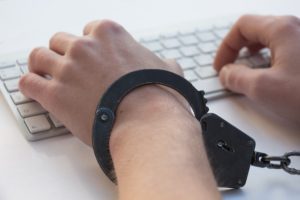 man in handcuffs at computer - representing computer fraud