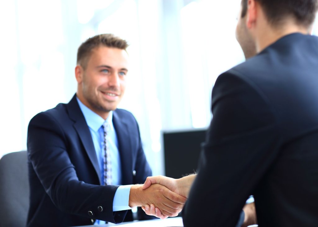 Male business man in a blue suit, shaking hands with a client after an introduction meeting
