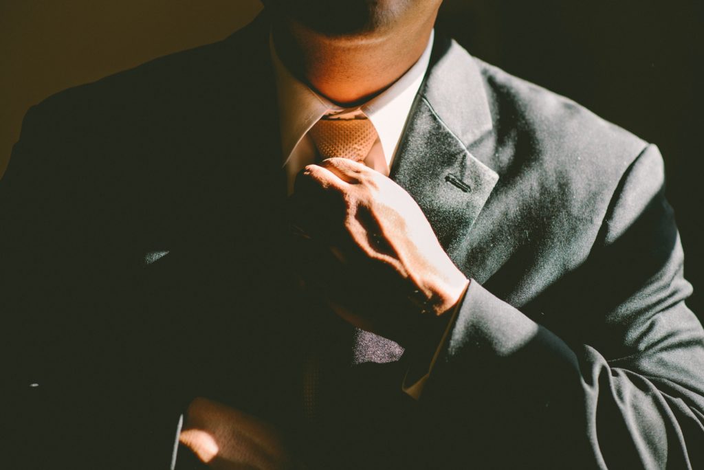 Male dressed in a gray suit, tightening natural printed tie with hands