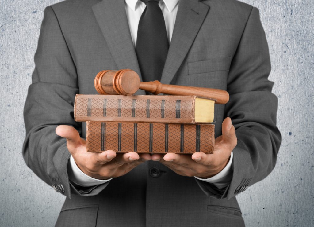 Male lawyer in a gray suit with black tie holding law books and gavel