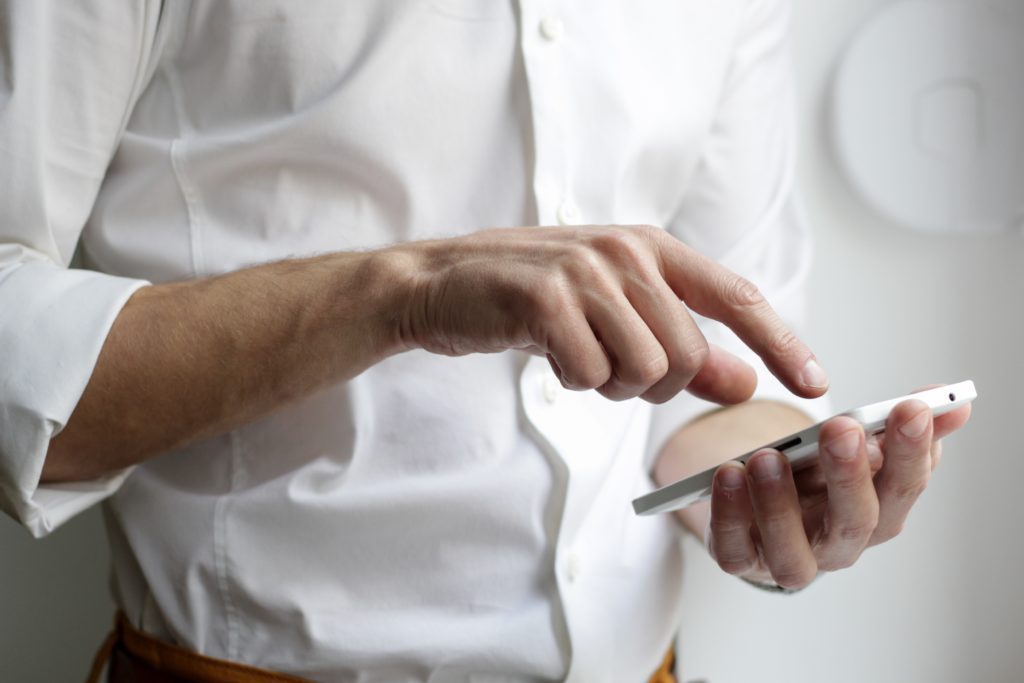 Male in a white button-up dress shirt holding a smartphone and scrolling through social media