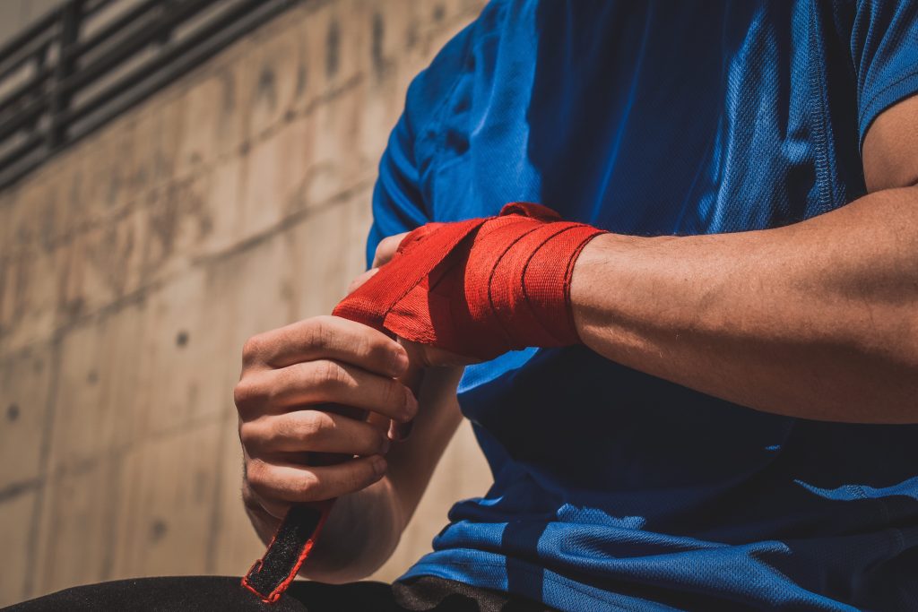 Male in blue shirt, wrapping hand with red cast/bandage after an injury to protect from infection