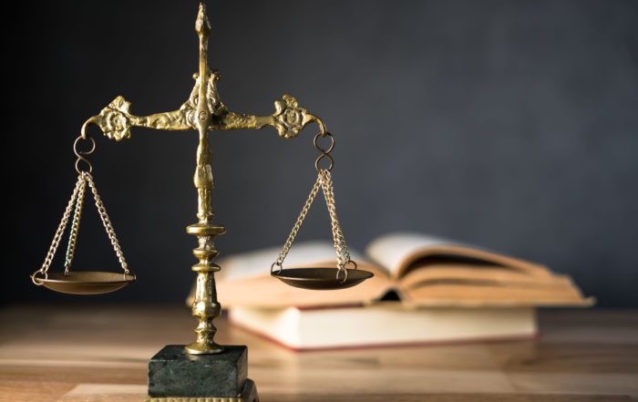 A close-up image of a brass balance scale, symbolizing justice, with a pair of open books in the background.