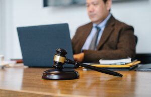 A gavel on a table with a man using a laptop in the background preparing for the bar exam