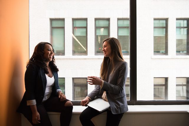 Two women talking sitting on a window ledge