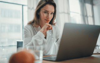 Female paralegal sits at a desk studying information on her laptop while holding her glasses